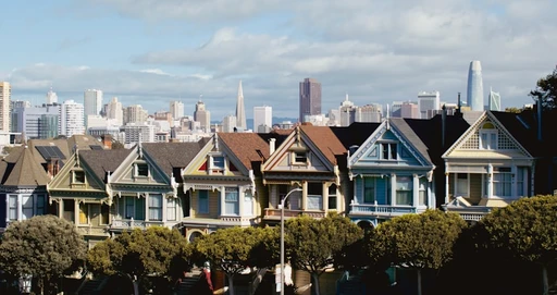 Row of colorful Victorian houses with a city skyline at dusk